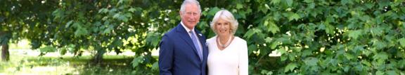 King Charles and Queen Camellia posing in front of a tree in a garden.