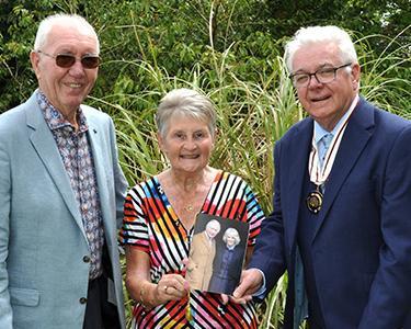 A man awards a couple with an award outside in a garden.