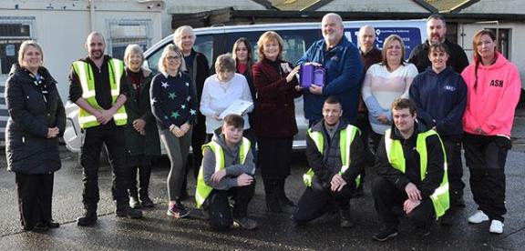 A group of people, some in hi-vis jacket, pose outside holding an award.