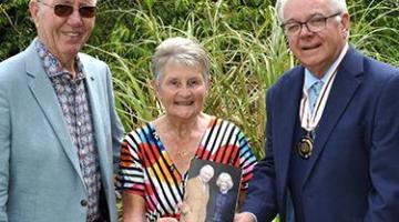 A man awards a couple with an award outside in a garden.