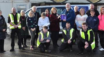 A group of people, some in hi-vis jacket, pose outside holding an award.